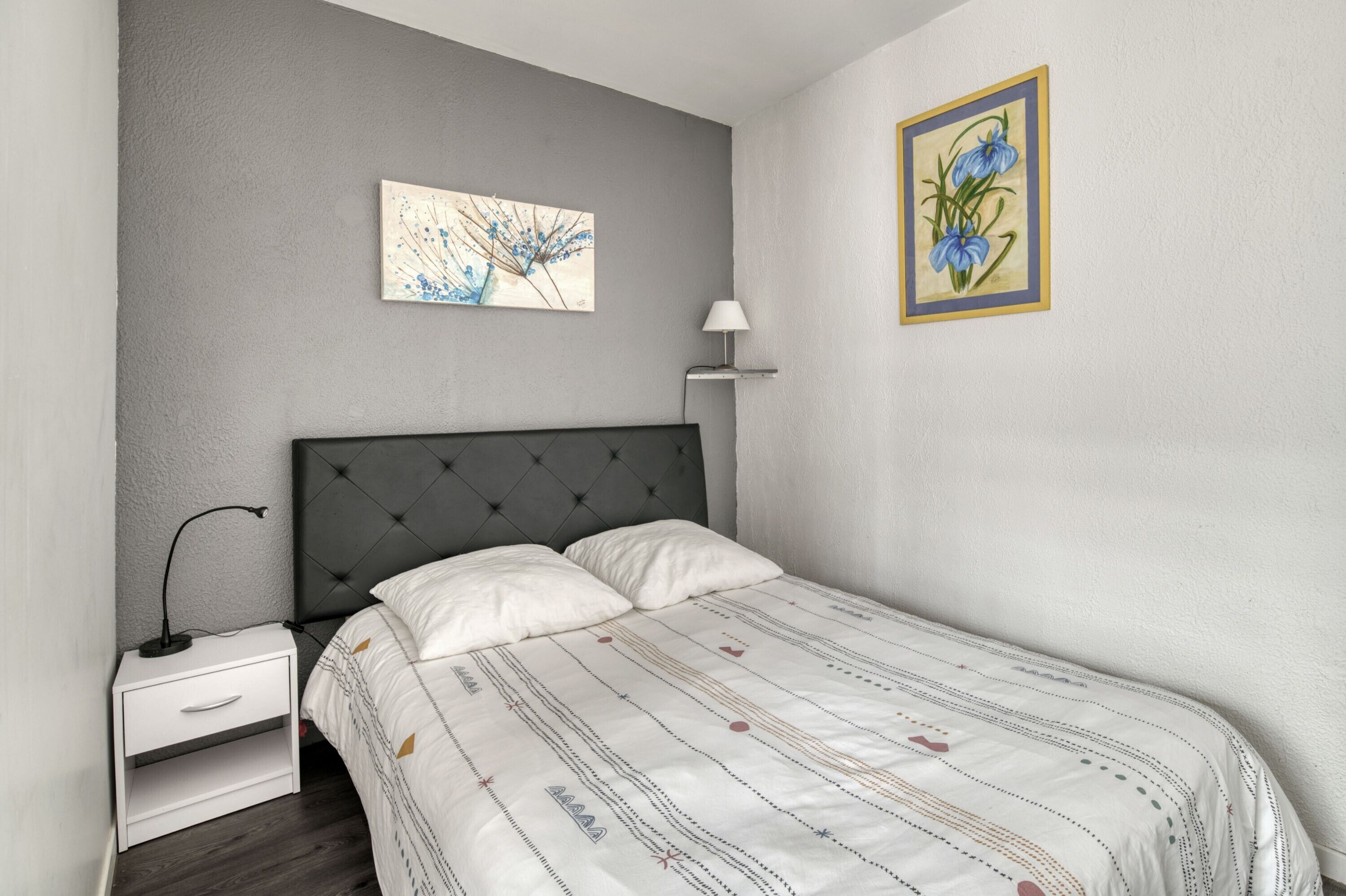 Ein Schlafzimmer mit einem Bett, einem Nachttisch, einer Lampe und zwei an der Wand befestigten Kunstwerken.