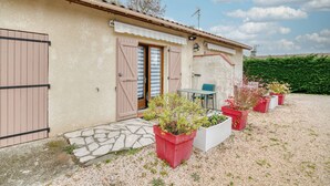 A house with a stone entrance, a small patio with a table and chairs, and potted plants. - Studio Apartment 'Le Laurier' with Private Terrace, Shared Garden and Wi-Fi (Lherm)