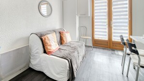 A room with a bed, a chair, a table, a radiator, a mirror, and a door with blinds. - Studio Apartment 'Le Laurier' with Private Terrace, Shared Garden and Wi-Fi (Lherm)