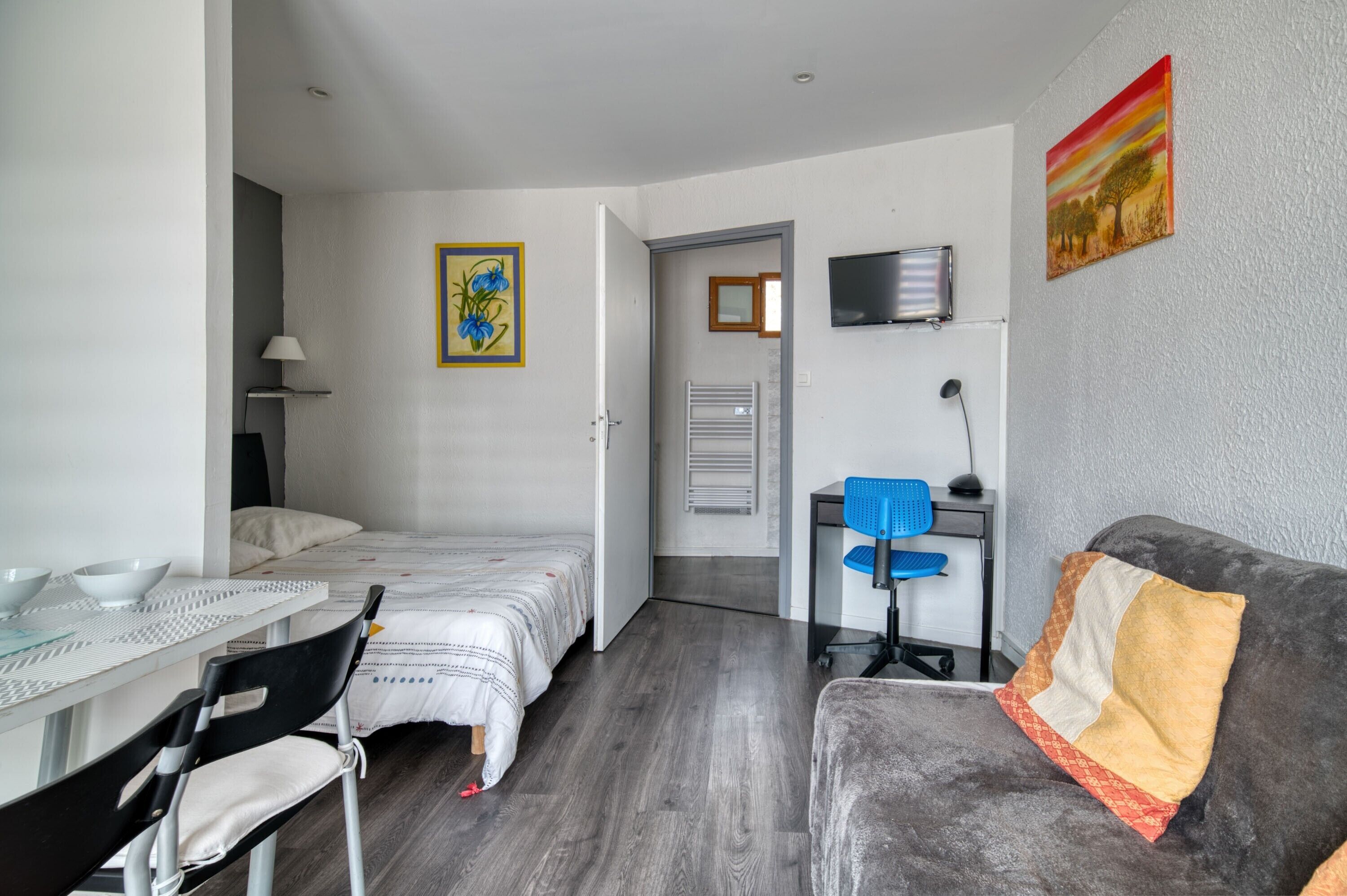 A room with a bed, a desk, a chair, a TV, and a painting on the wall.