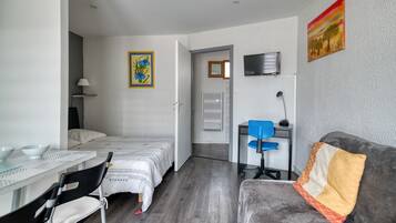 A room with a bed, a desk, a chair, a TV, and a painting on the wall.