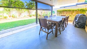 An outdoor patio with a table and chairs, a covered grill, and a view of a garden.