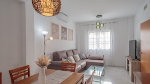 A modern living room with a sofa, dining table, chairs, a TV, and decorative elements. - Holiday Home 'El Rincón Sevillano' with Private Terrace, Wi-Fi and Air Conditioning (Gerena)