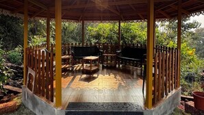 A covered outdoor seating area with wooden furniture and steps leading up to it. - The Alphonso Mango County (Anjarle)