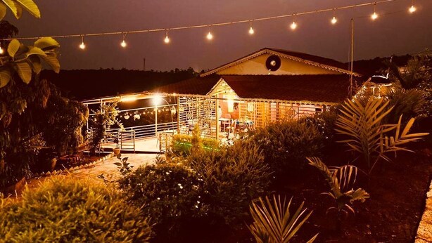 A building with a covered outdoor area, surrounded by vegetation and string lights. - The Alphonso Mango County (Anjarle)