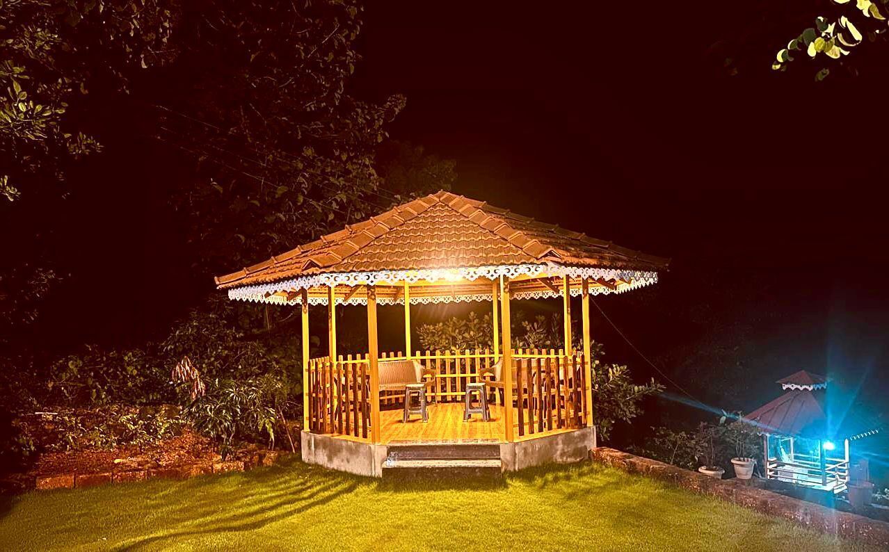 A gazebo with a tiled roof and a wooden railing, surrounded by a well-maintained lawn and trees.