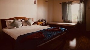 A bedroom with a bed, pillows, a bedside table, a chair, and a window with curtains. - The Alphonso Mango County (Anjarle)