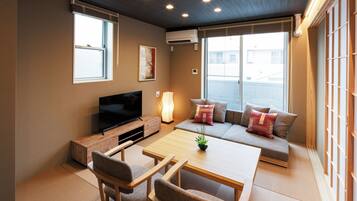 A modern living room with a flat-screen TV, a sofa with cushions, a coffee table, and a potted plant.