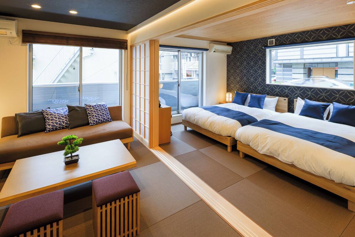 Une chambre d’hôtel moderne, équipée d’un canapé, de deux lits, d’une petite table avec une plante et offrant une vue sur l’extérieur.