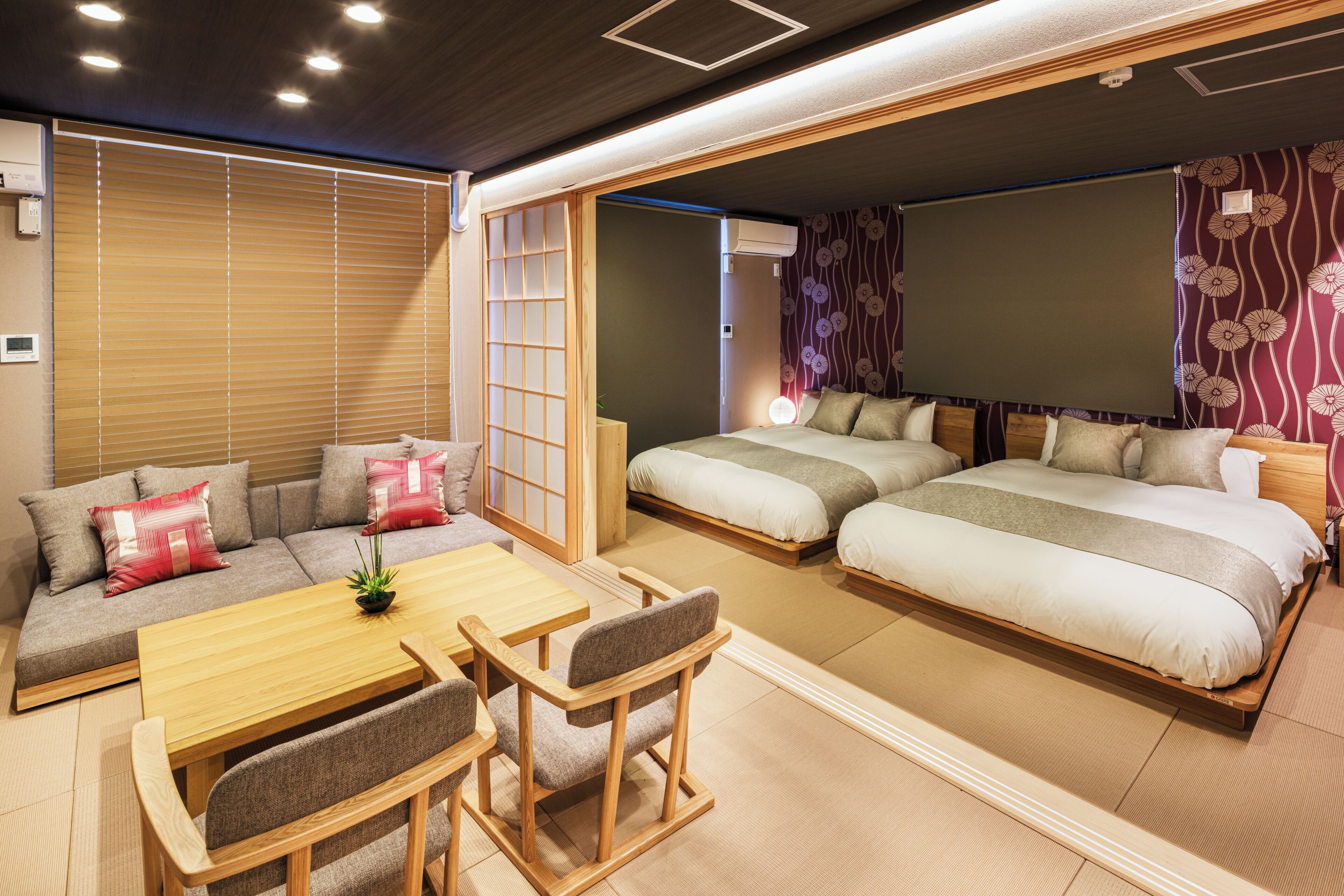 A traditional Japanese-style room with tatami flooring, a low table with chairs, a sofa, and two beds with futons.