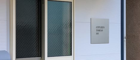 Une fenêtre munie d’une moustiquaire métallique et d’une enseigne indiquant « CITYZEN TOKYO 101 ».