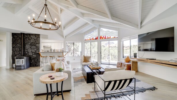 A spacious living area with a modern chandelier, a stone wall, a kitchen, and a large TV. - Walk to Park & Trails! Mtn-view Sedona Haven (Sedona)