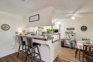A modern kitchen with a bar area, wooden flooring, and a ceiling fan. - Home w/ Backyard Oasis < 7 Mi to At&t Stadium! (Euless)