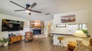 A living room with a fireplace, a ceiling fan, a TV, and a bar area. - Home w/ Backyard Oasis < 7 Mi to At&t Stadium! (Euless)