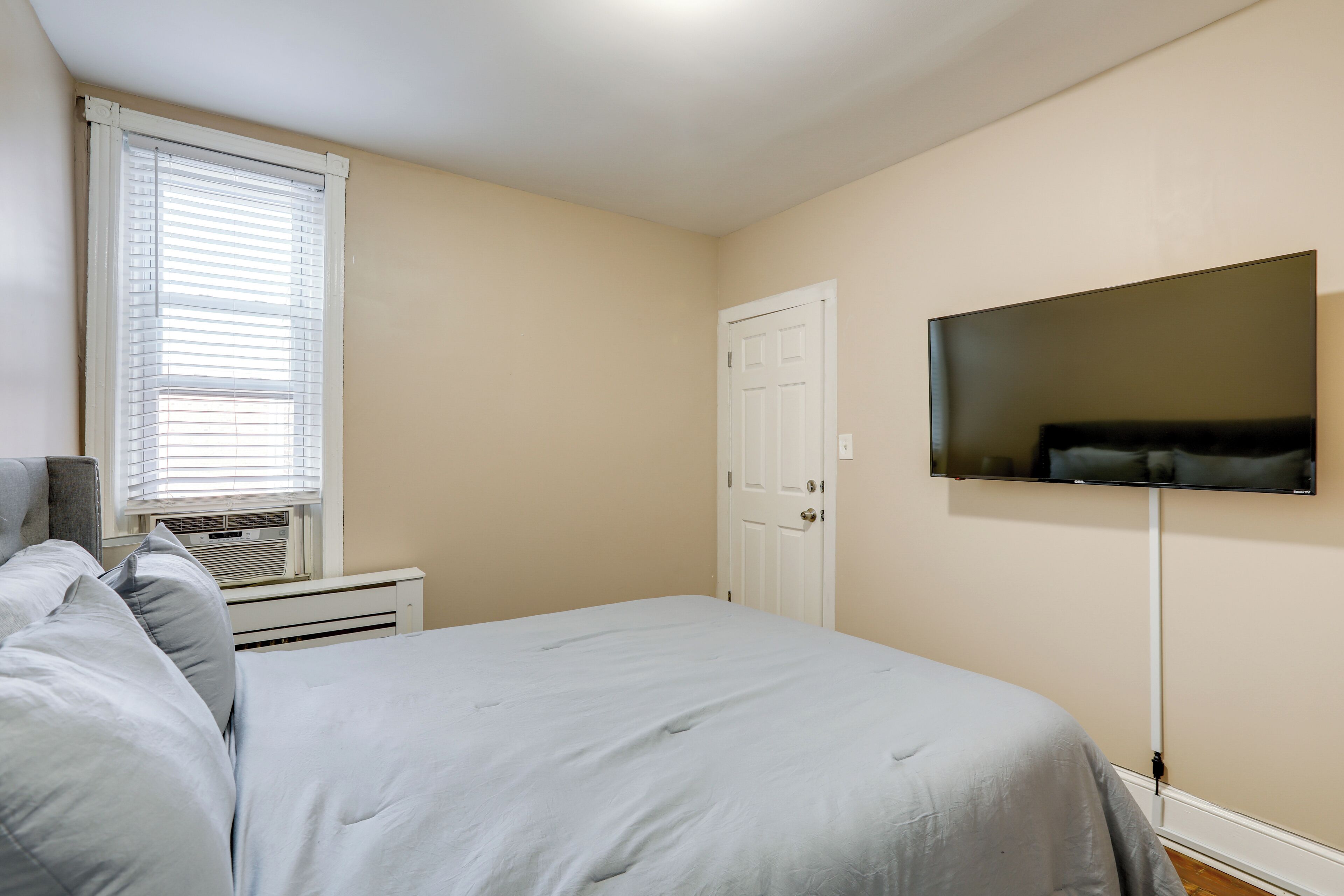 Una camera da letto con un letto, una TV a parete, una finestra con persiane e una porta.