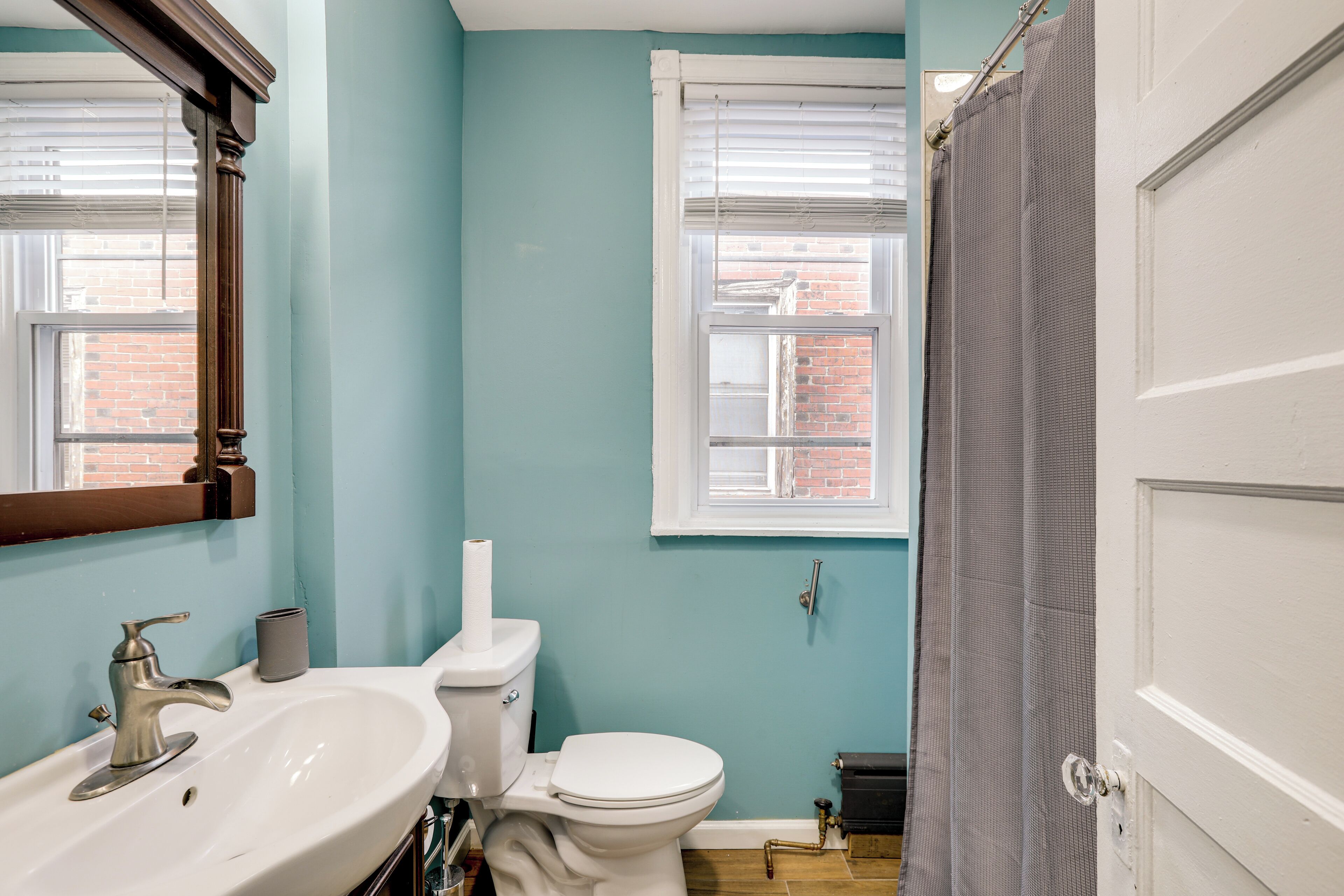 Une salle de bain avec un lavabo blanc, des toilettes et une fenêtre avec des stores.