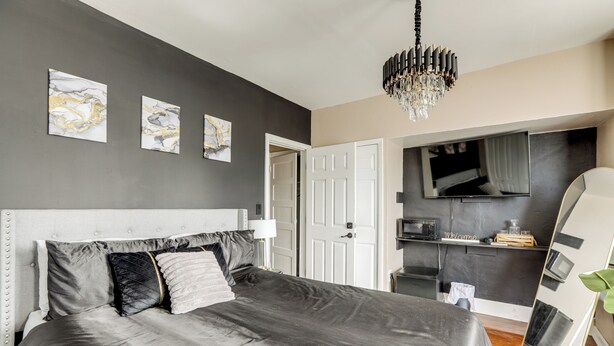 A modern bedroom with a large bed, a chandelier, and artwork on the wall. - Private Backyard Jawn! Multi-level Philly Rowhouse (Philadelphia)