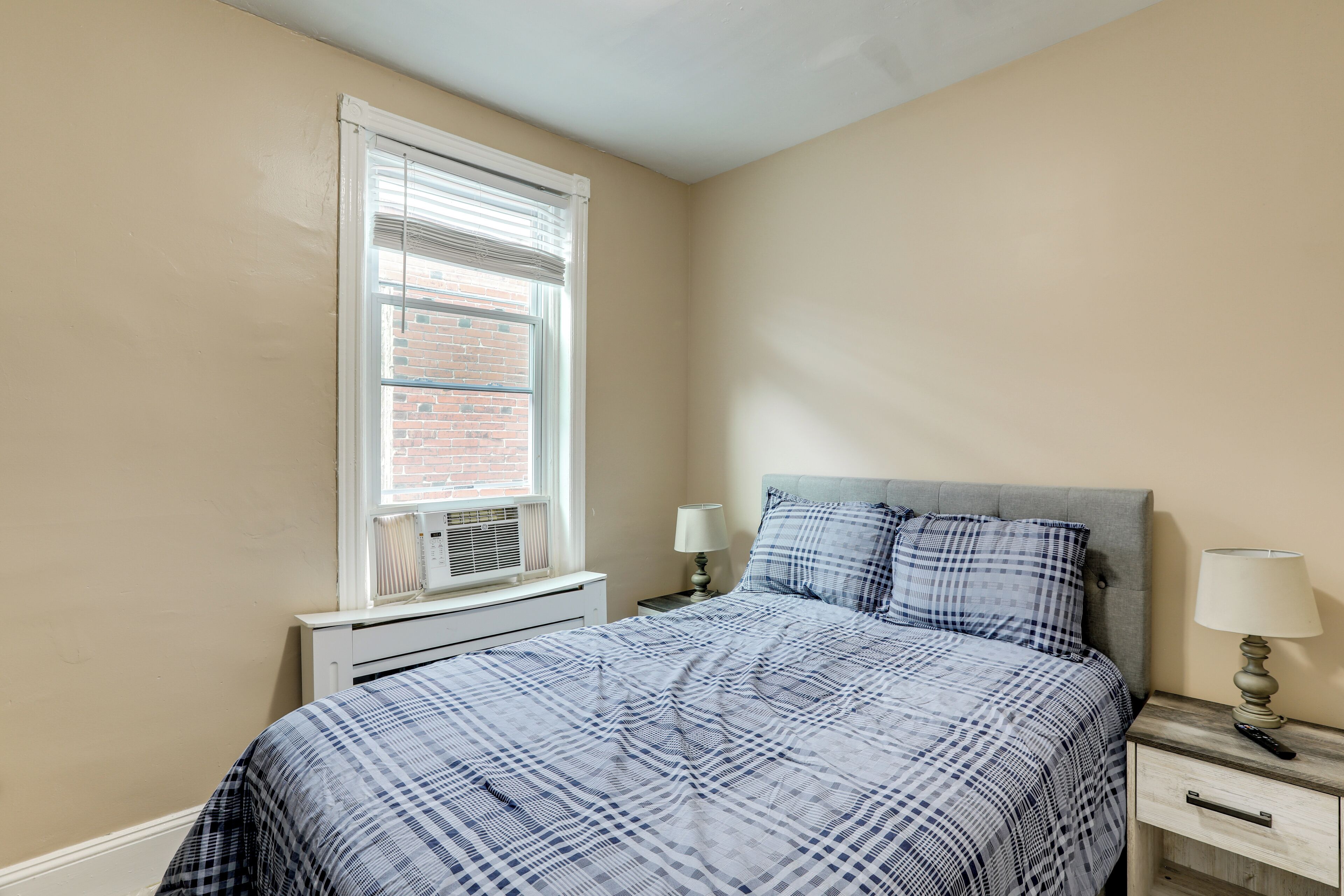 Une chambre à coucher avec un lit, une table de chevet, une lampe, une fenêtre et un radiateur.