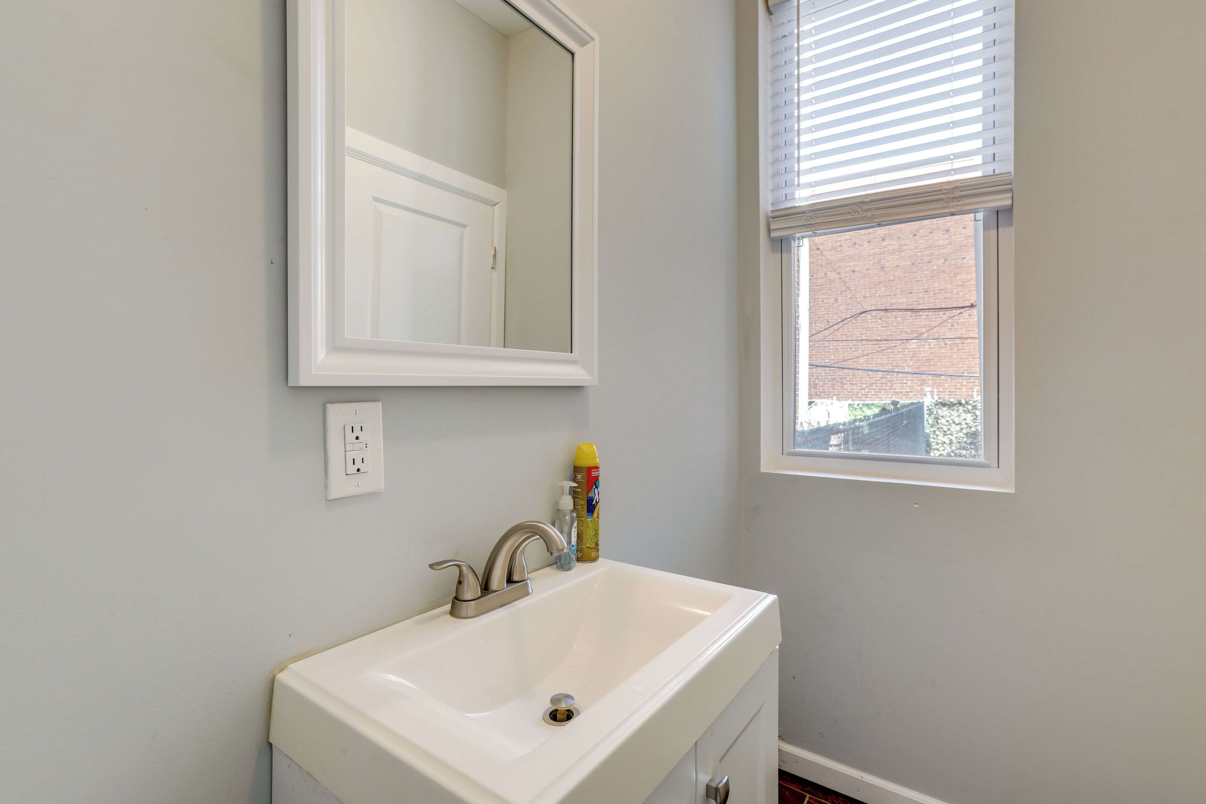 A bathroom with a white sink, a mirror, and a window with blinds.