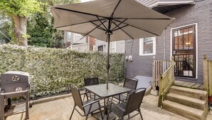 An outdoor patio with a table and chairs, a grill, and a large umbrella. - Private Backyard Jawn! Multi-level Philly Rowhouse (Philadelphia)