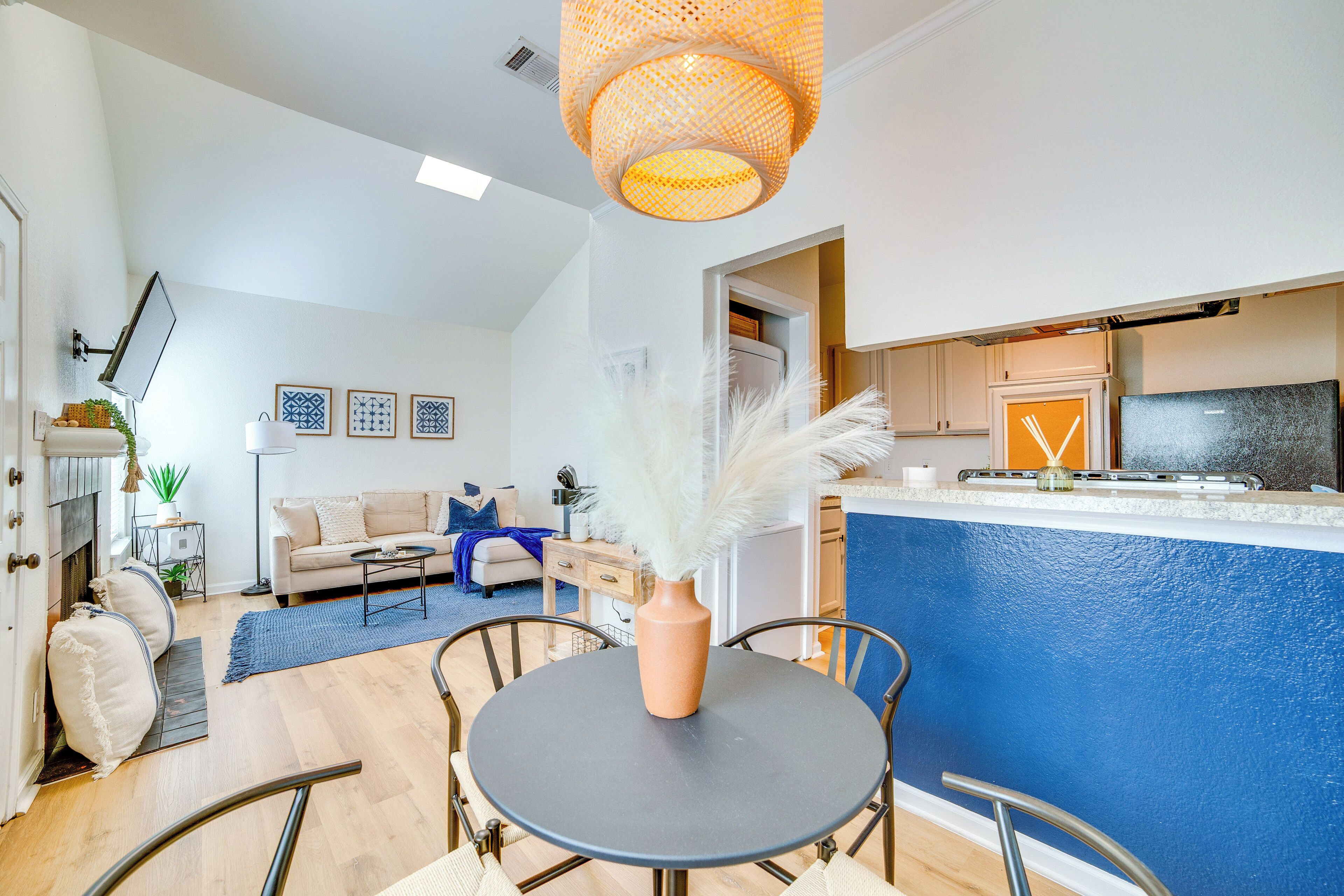 Eine moderne Küche mit blauer Akzentwand, ein Essbereich mit rundem Tisch und ein Wohnzimmer mit Sofa und dekorativen Kissen.