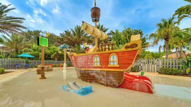 A pirate ship play area with a slide, surrounded by palm trees and a fence. - Fall Family Fun Near Disney! Resort Perks & Golf (Davenport)