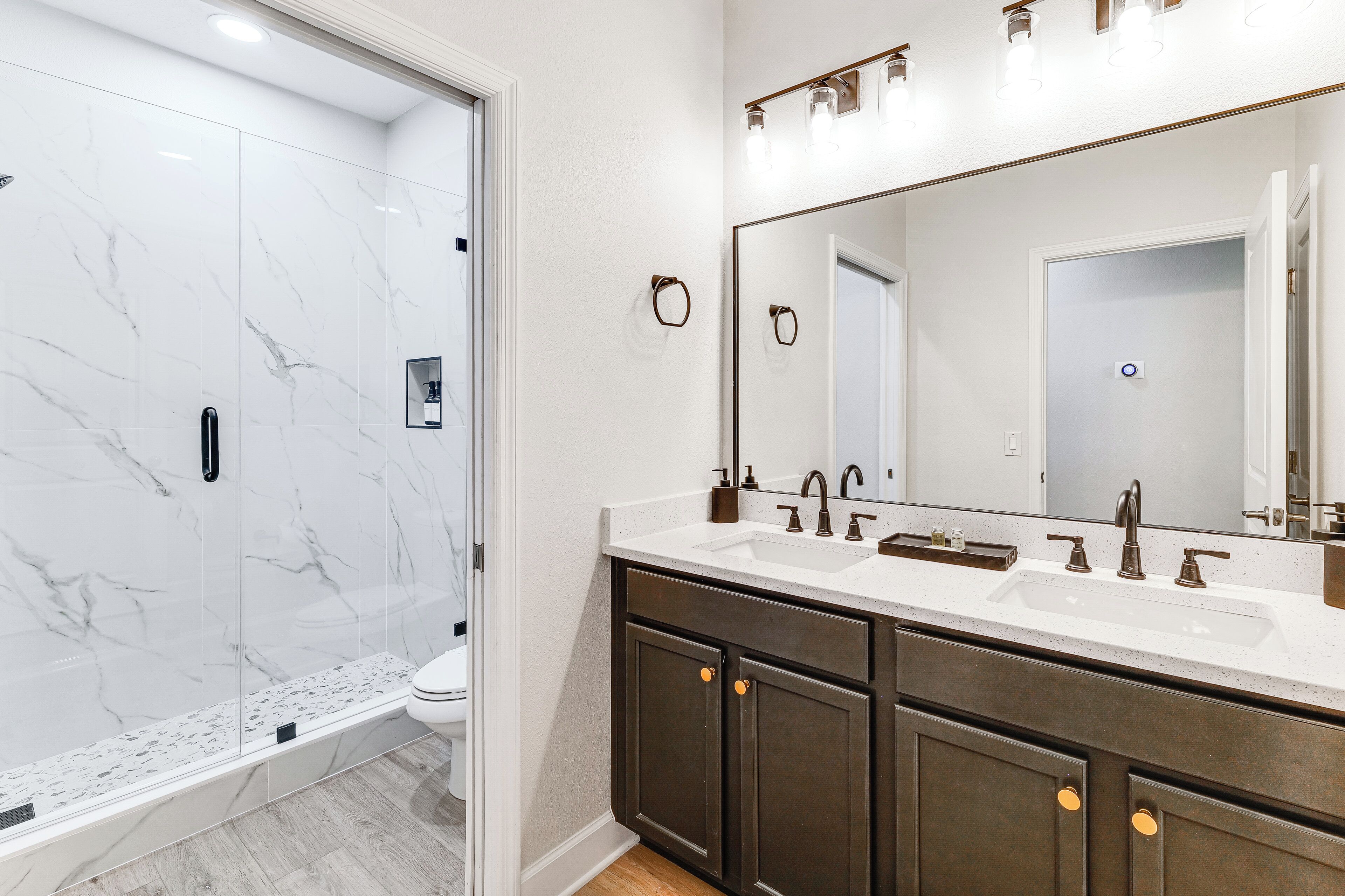 Une salle de bain moderne avec une douche à parois de verre, un grand miroir et des meubles en bois foncé.