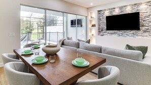 A modern living room with a wooden dining table, grey upholstered sofa, and a stone-patterned wall. - Fall Family Fun Near Disney! Resort Perks & Golf (Davenport)