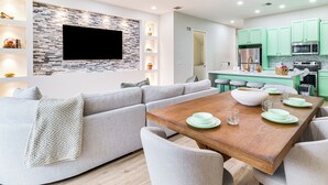 A modern living room with a sofa, a wooden dining table set with green plates, and a kitchen with green cabinets. - Fall Family Fun Near Disney! Resort Perks & Golf (Davenport)