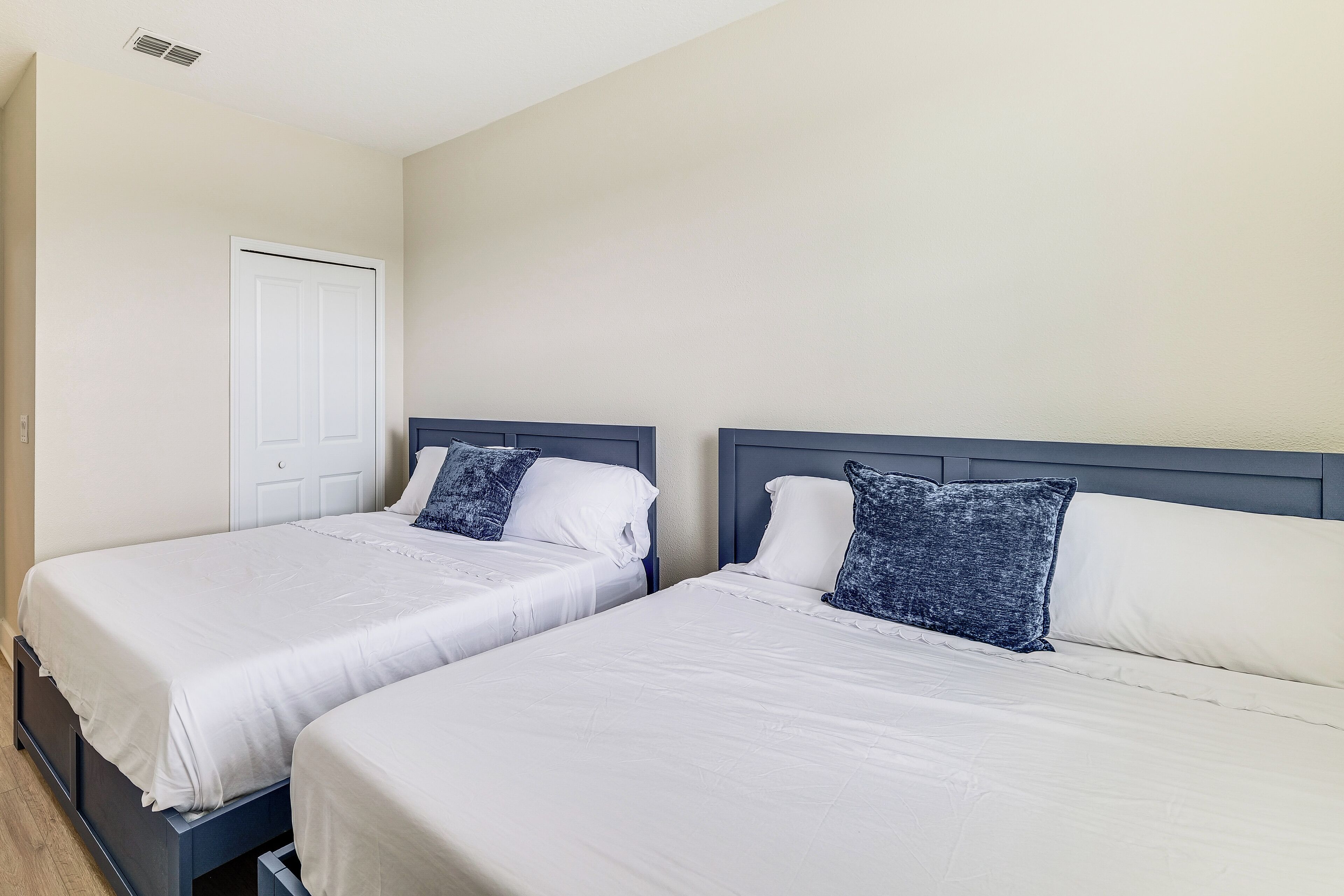 Two single beds with white linens and dark headboards in a room with beige walls and a white door.
