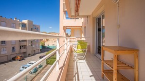 A balcony with a wooden table, chairs, and a view of a parking lot and buildings. - Apartment "400m from the Beach" with Balcony (Fréjus)