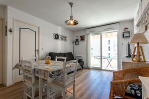 Uma sala de jantar com mesa e cadeiras, um sofá, um abajur e vista para o exterior através de uma porta de vidro.