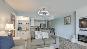 A living room with a sofa, a coffee table, and a TV. There is a kitchen in the background. - Direct Beach Access! Walkable Condo on Ocean Blvd (North Myrtle Beach)