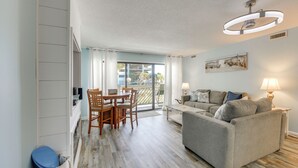 A living room with a sofa, a dining table with chairs, a ceiling light, and a view through a glass door. - Direct Beach Access! Walkable Condo on Ocean Blvd (North Myrtle Beach)