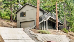 Une maison moderne à deux étages avec un garage, entourée d’arbres et dotée d’un escalier en pierre menant à l’entrée.