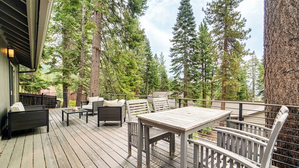 Une terrasse en bois, agréée de mobilier d’extérieur, entourée de grands arbres.