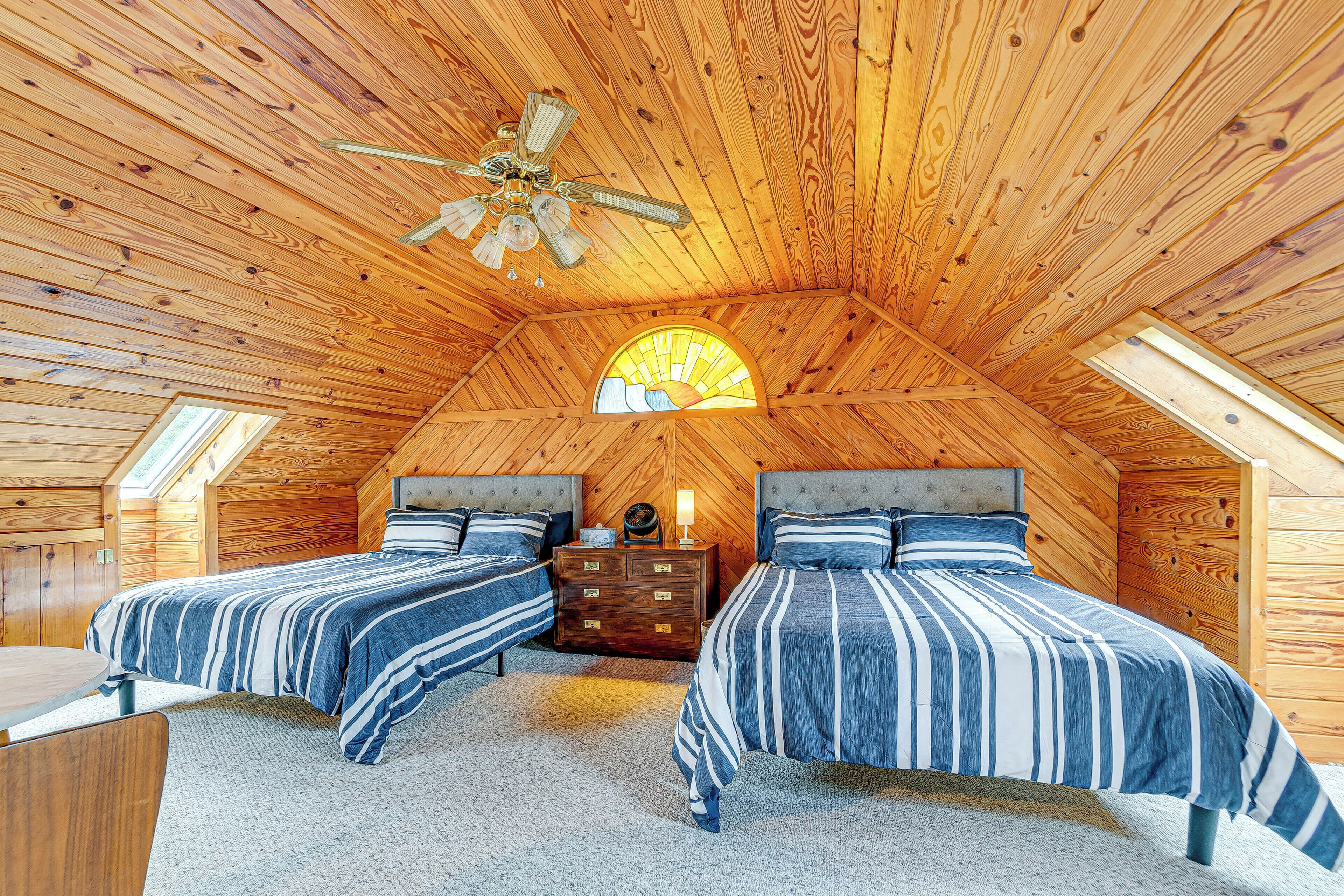 A cozy attic bedroom with two beds, a ceiling fan, and a skylight.