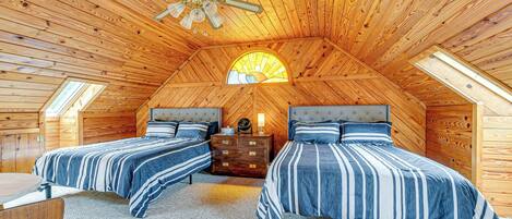 A cozy attic bedroom with two beds, a ceiling fan, and a skylight.