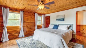 Une chambre dans une cabane en bois, avec un lit, des rideaux, un ventilateur de plafond et un tapis.