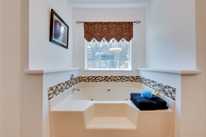A bathroom with a large bathtub, a window with a patterned valance, a tiled backsplash, and a framed picture on the wall. - Unwind, Golf & Explore: Unique Atlanta Escape! (Atlanta)