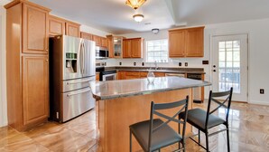 A spacious kitchen with wooden cabinets, stainless steel appliances, and a large island with two chairs. - Unwind, Golf & Explore: Unique Atlanta Escape! (Atlanta)