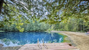 Une jetée en bois mène à un lac aux eaux d’un bleu limpide, entouré d’une forêt dense.