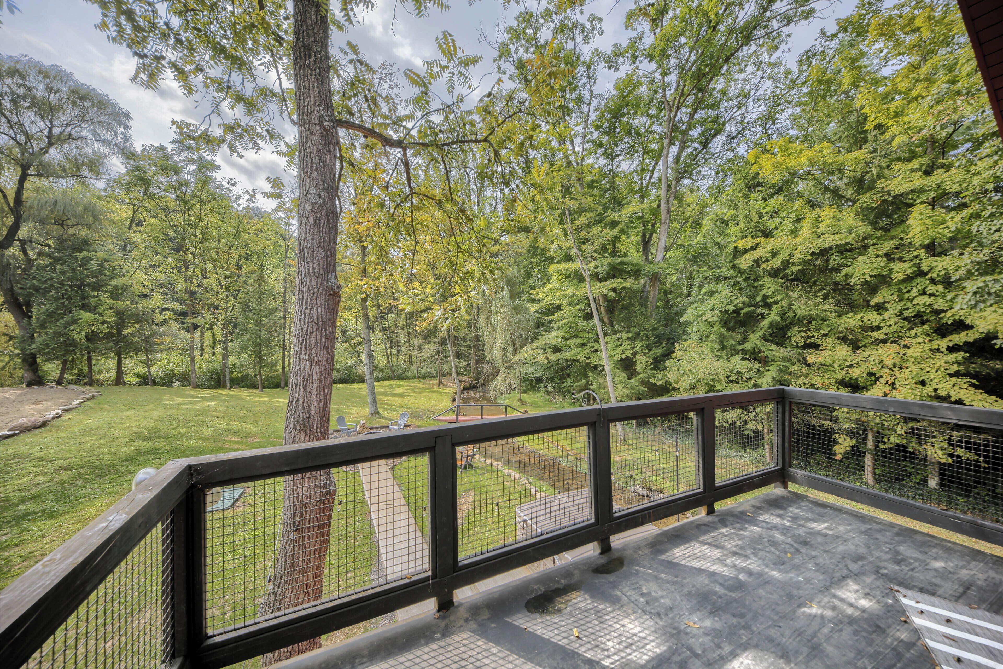 A wooden deck with a metal railing overlooking a grassy area with trees.