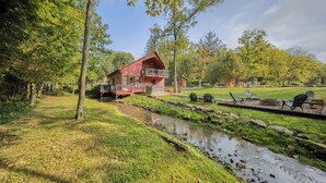 Une cabane avec un balcon, un petit ruisseau et un espace salon extérieur.