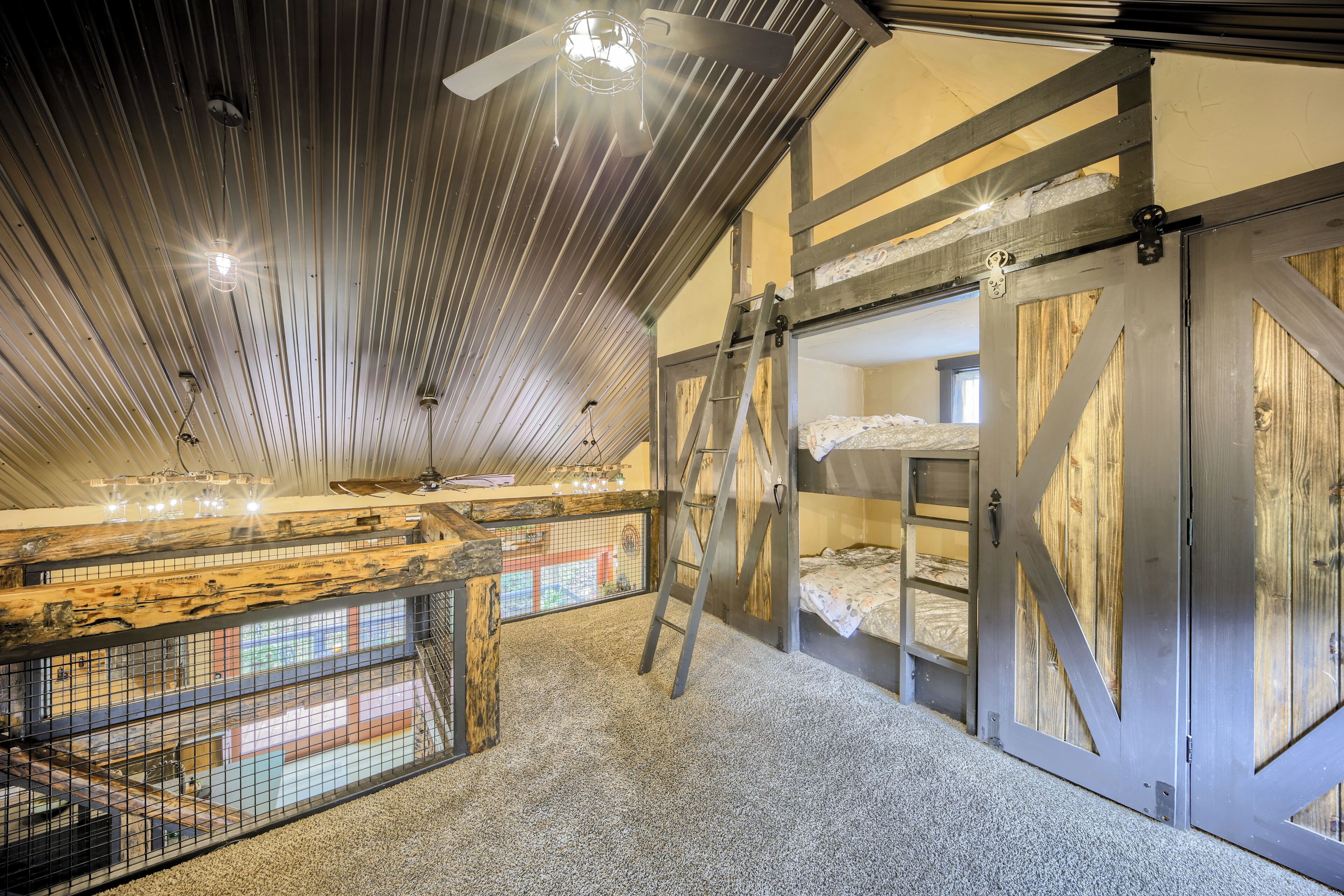 A high-ceilinged room with a ladder, bunk beds, and a view through a mesh window.