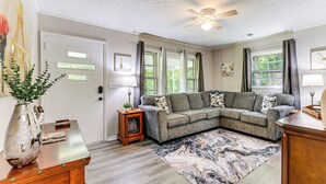 A living room with a sectional sofa, a wooden coffee table, a floor lamp, and a large window with curtains.