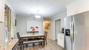 A modern kitchen with a stainless steel refrigerator, wooden dining table, and a clock on the wall.