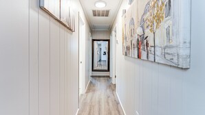 A hallway with wooden flooring, white walls, and a painting on the right.