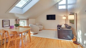 Une chambre spacieuse aménagée en mezzanine, dotée d’une lucarne, d’un grand lit, d’un bureau et d’une chaise.