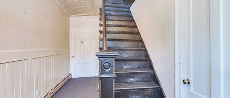 A staircase with a handrail, a door at the bottom, and a light fixture on the ceiling.